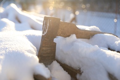 Metal axe on snowy firewood outdoors on sunny winter day, closeup