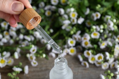 Photo of Woman pouring chamomile essential oil from pipette into bottle on table, closeup. Space for text