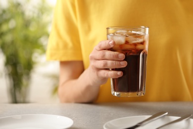 Woman holding glass of cola with ice at table, closeup. Space for text