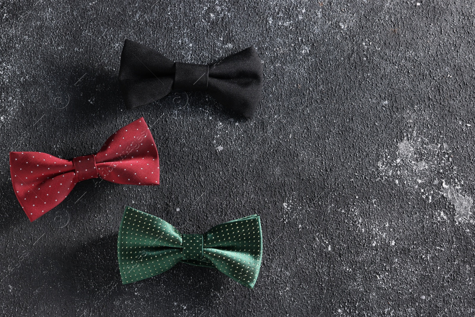 Photo of Stylish color bow ties on black textured background, flat lay. Space for text