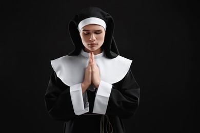 Nun with clasped hands praying to God on black background