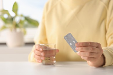 Photo of Woman taking emergency contraception pill at white table indoors, focus on hand