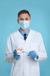 Photo of Dentist with jaws model and toothbrush on light blue background. Oral care demonstration