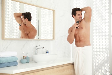 Handsome young man applying deodorant in bathroom