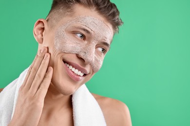 Photo of Handsome man applying facial mask onto his face on green background. Space for text