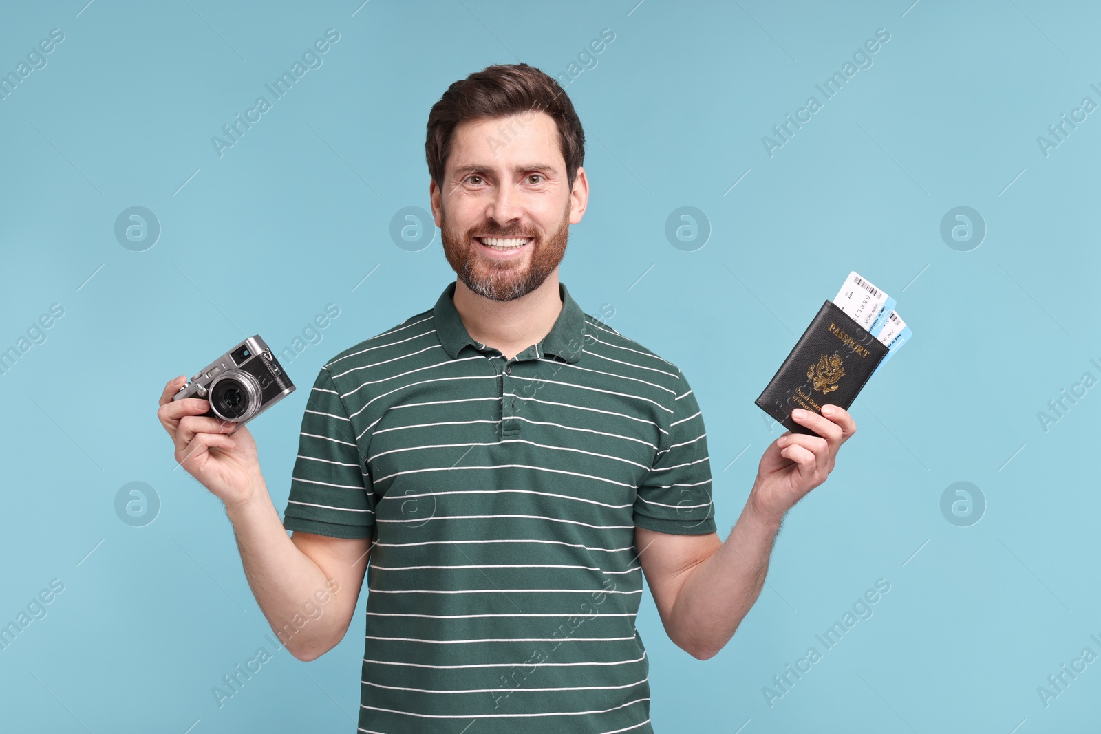 Photo of Smiling man with passport, camera and tickets on light blue background