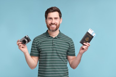 Photo of Smiling man with passport, camera and tickets on light blue background