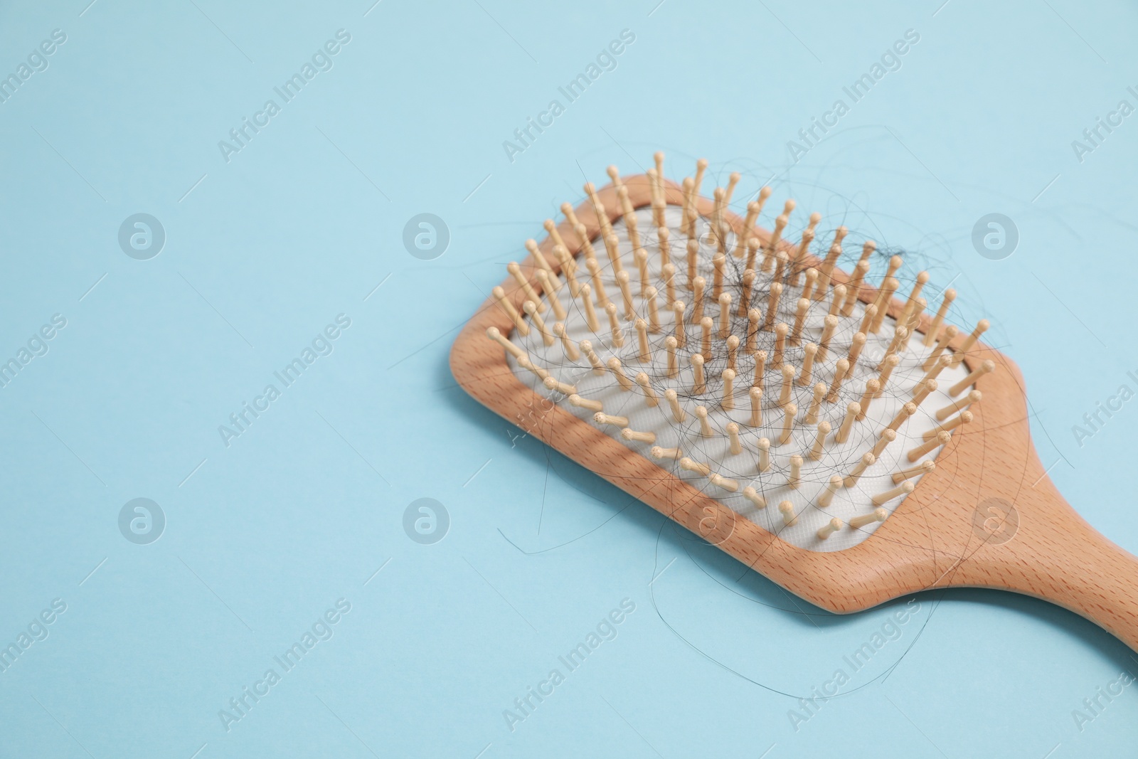 Photo of Wooden brush with lost hair on light blue background, closeup. Space for text