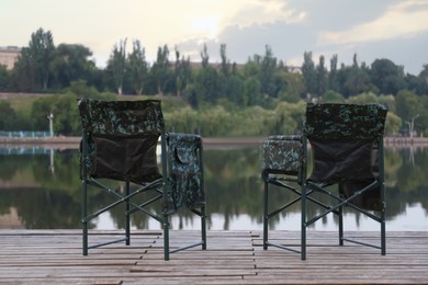 Camouflage fishing chairs on wooden pier near river