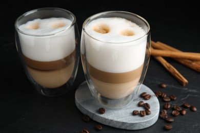 Delicious latte macchiato, cinnamon sticks and coffee beans on black table