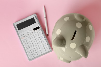 Piggy bank, calculator and pen on pink background, flat lay