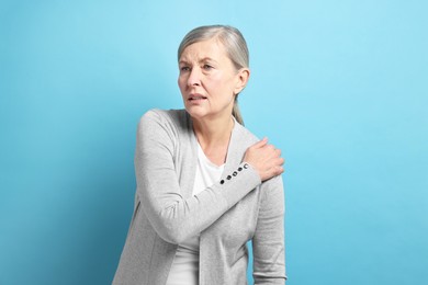 Photo of Arthritis symptoms. Woman suffering from pain in shoulder on light blue background