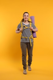 Photo of Smiling young woman with backpack walking on orange background. Active tourism