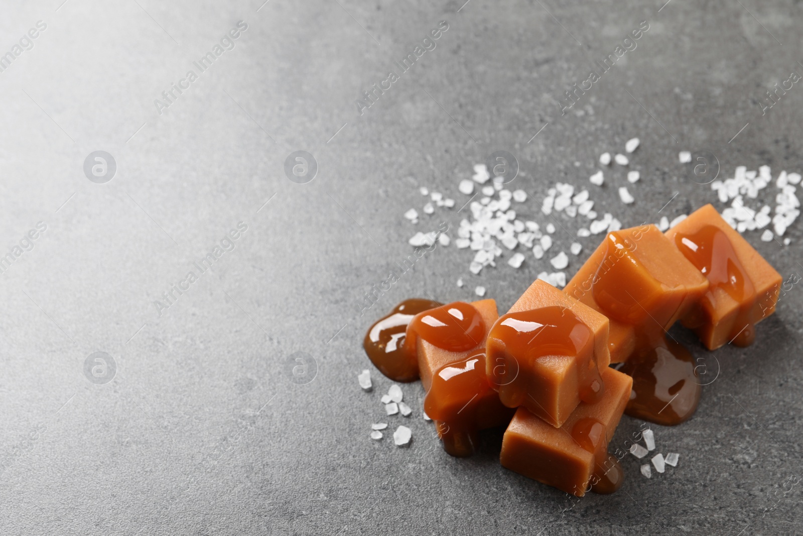 Photo of Yummy caramel candies with sauce and sea salt on grey table, space for text