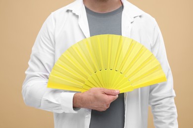 Photo of Man holding hand fan on beige background, closeup