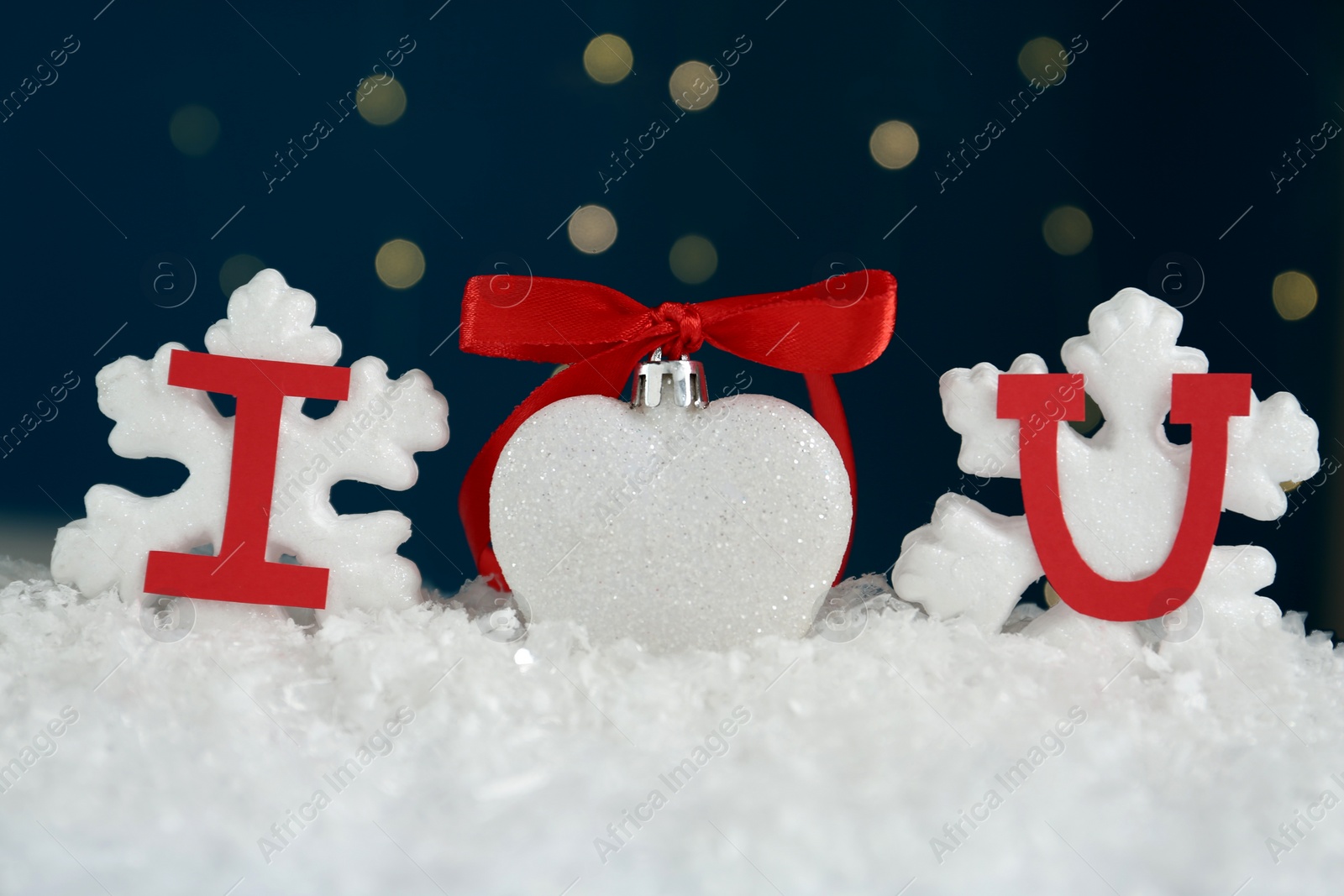 Photo of Phrase I Love You made of paper letters and festive heart shaped ornament on snow against blue background