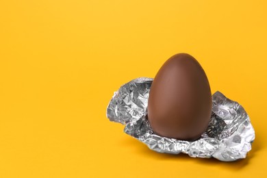 Photo of Tasty chocolate egg with foil on orange background. Space for text