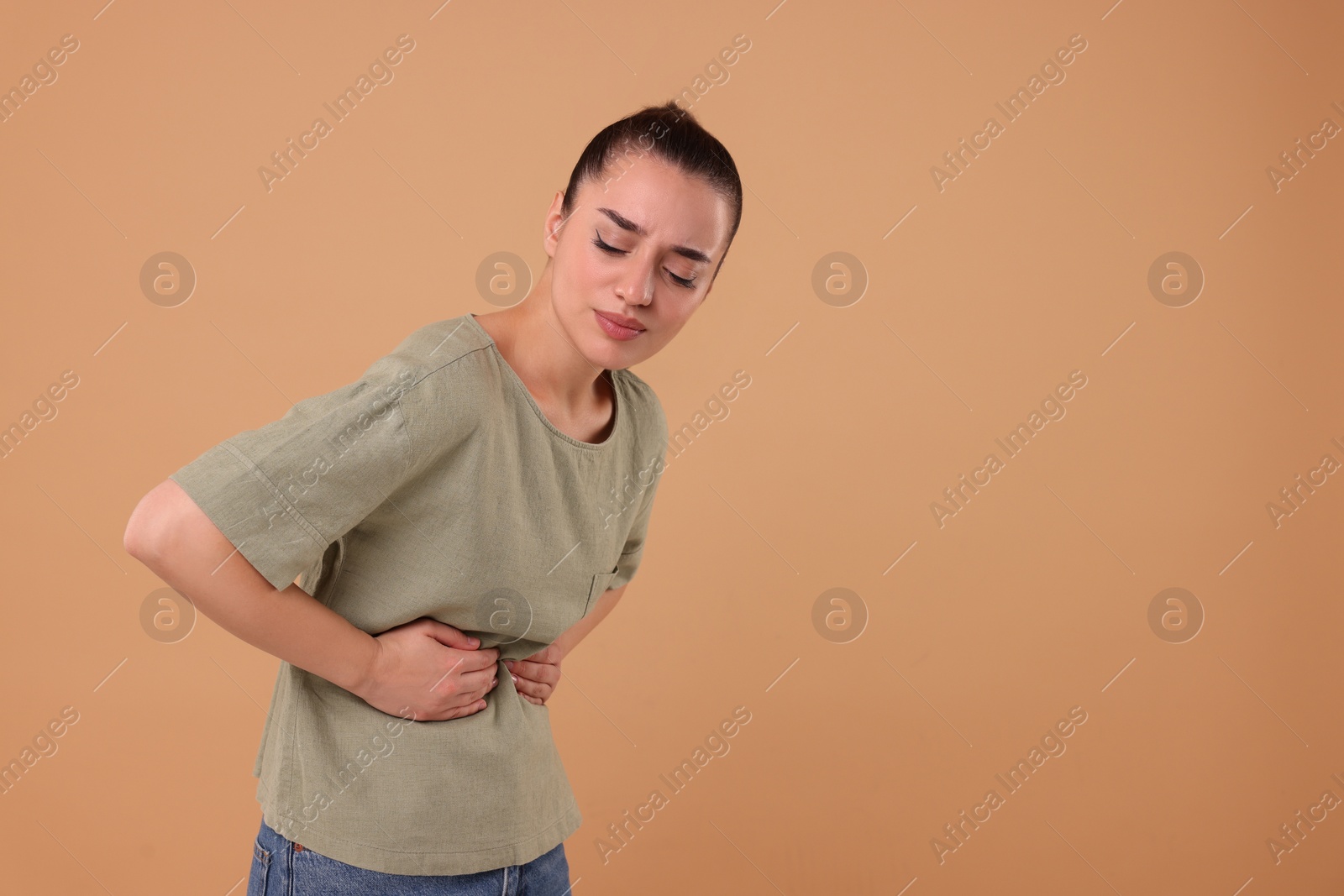 Photo of Woman suffering from abdominal pain on beige background, space for text. Unhealthy stomach