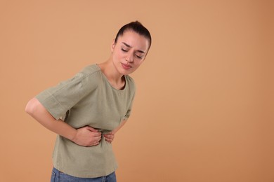 Photo of Woman suffering from abdominal pain on beige background, space for text. Unhealthy stomach