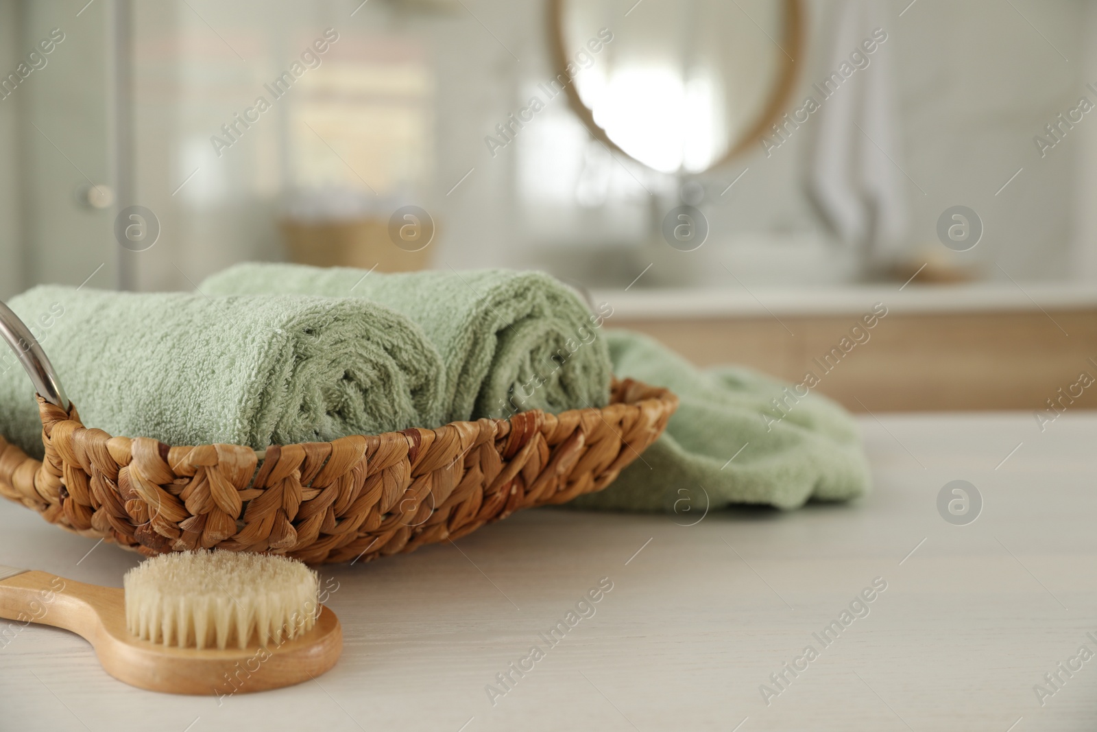 Photo of Wicker basket with rolled towels and massage brush on white wooden table in bathroom