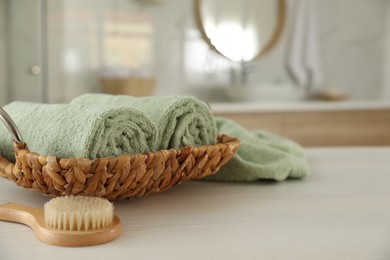 Wicker basket with rolled towels and massage brush on white wooden table in bathroom
