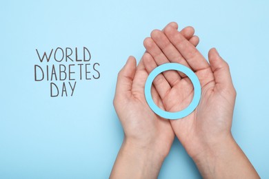 Woman holding blue paper circle near text World Diabetes Day on color background, top view