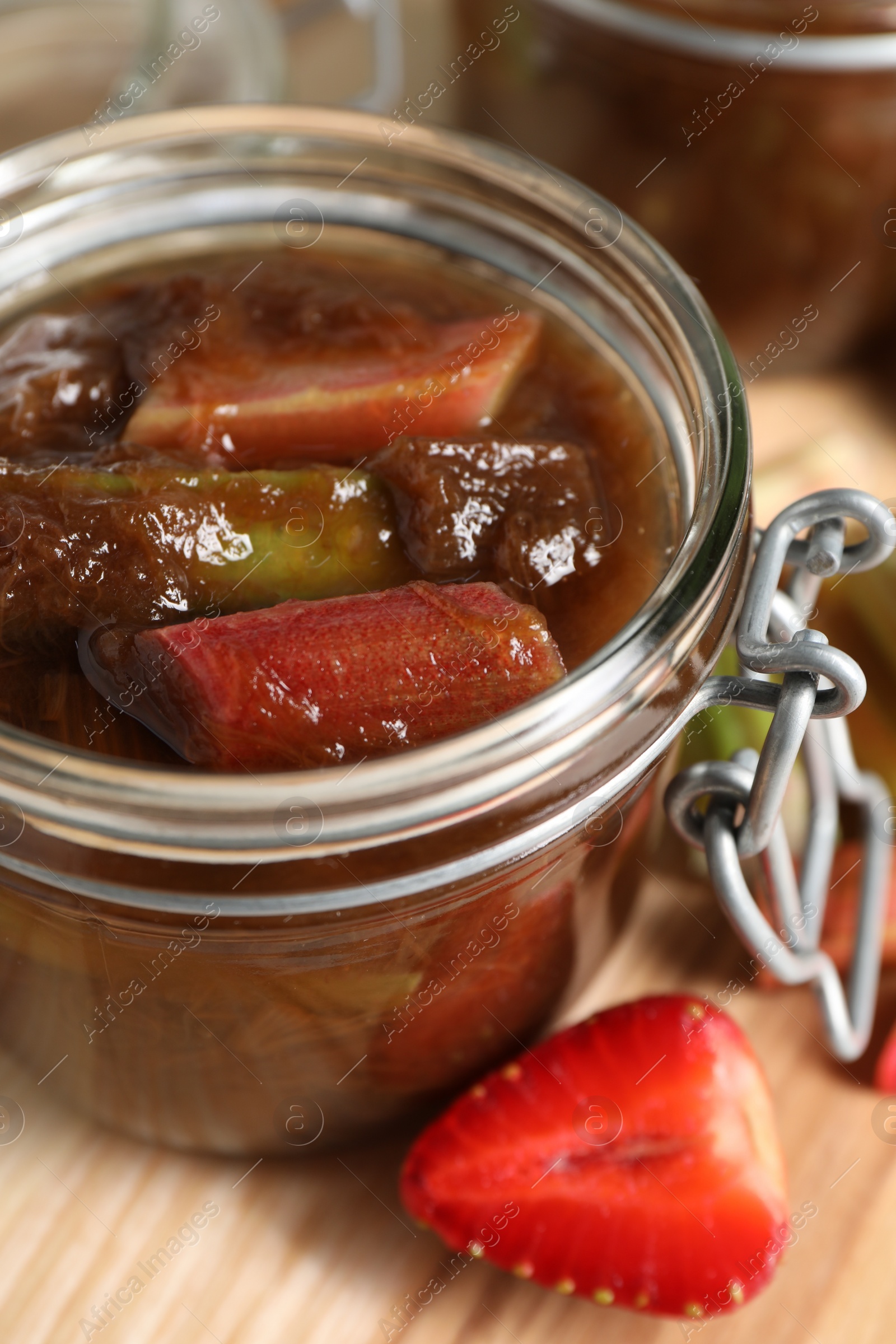 Photo of Jar of tasty rhubarb jam and strawberry on wooden table, closeup