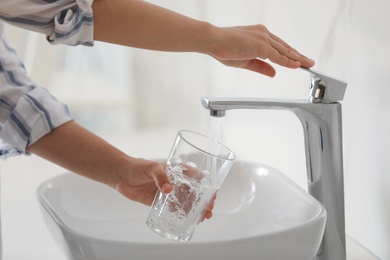 Photo of Woman filling glass with water from faucet over sink, closeup