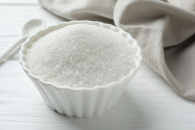 Photo of Granulated sugar in bowl on white wooden table, closeup