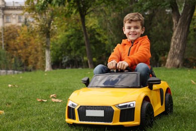 Cute little boy driving children's car in park. Space for text