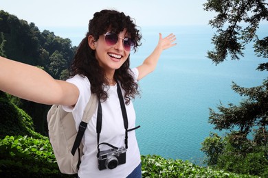 Image of Beautiful woman in sunglasses with camera taking selfie on hill near sea