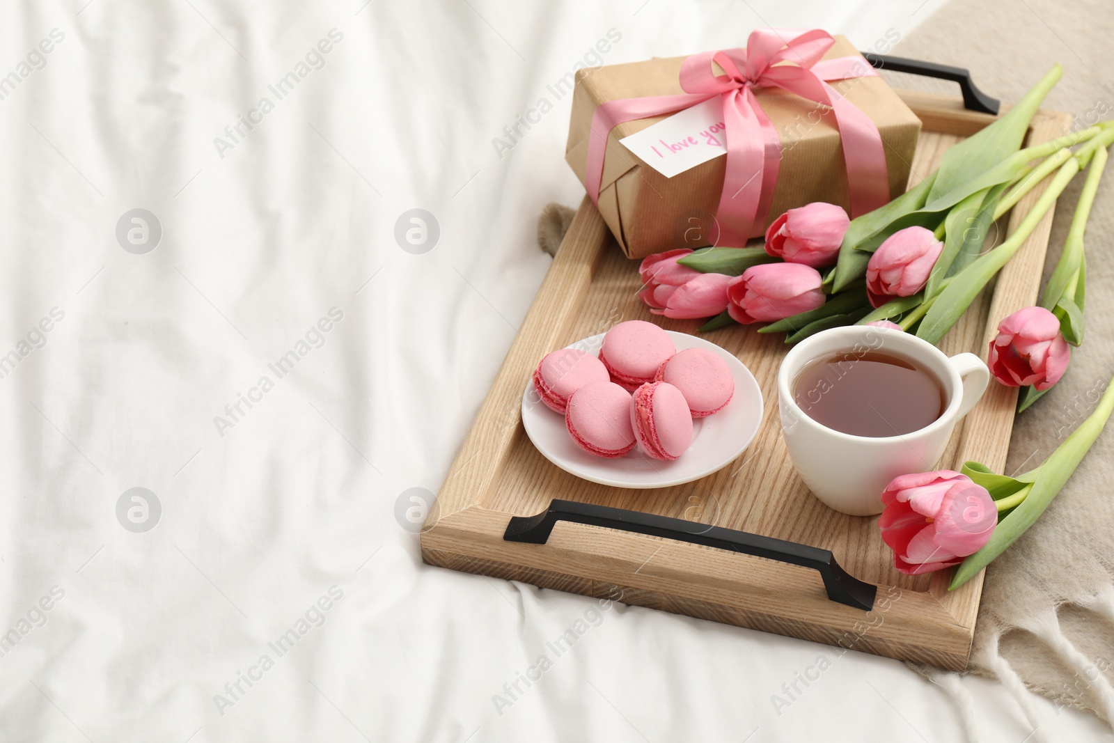 Photo of Tasty breakfast served in bed. Delicious macarons, tea, flowers, gift box and card with phrase I Love You on tray, space for text