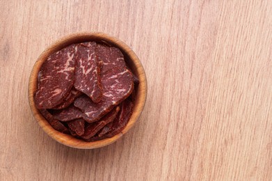 Photo of Delicious beef jerky in bowl on wooden table, top view, space for text