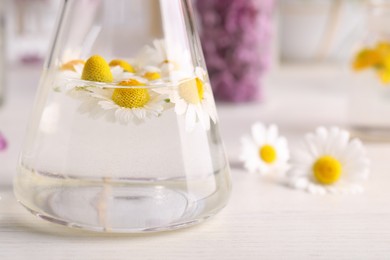 Photo of Flask with flowers on table, closeup. Extracting essential oil for perfumery and cosmetics