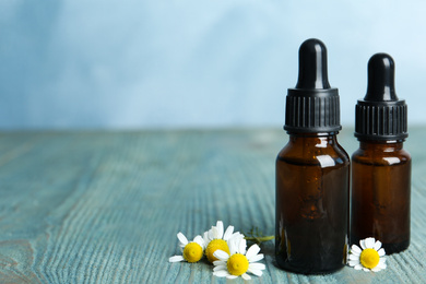 Bottles of essential oil and chamomiles on blue wooden table. Space for text