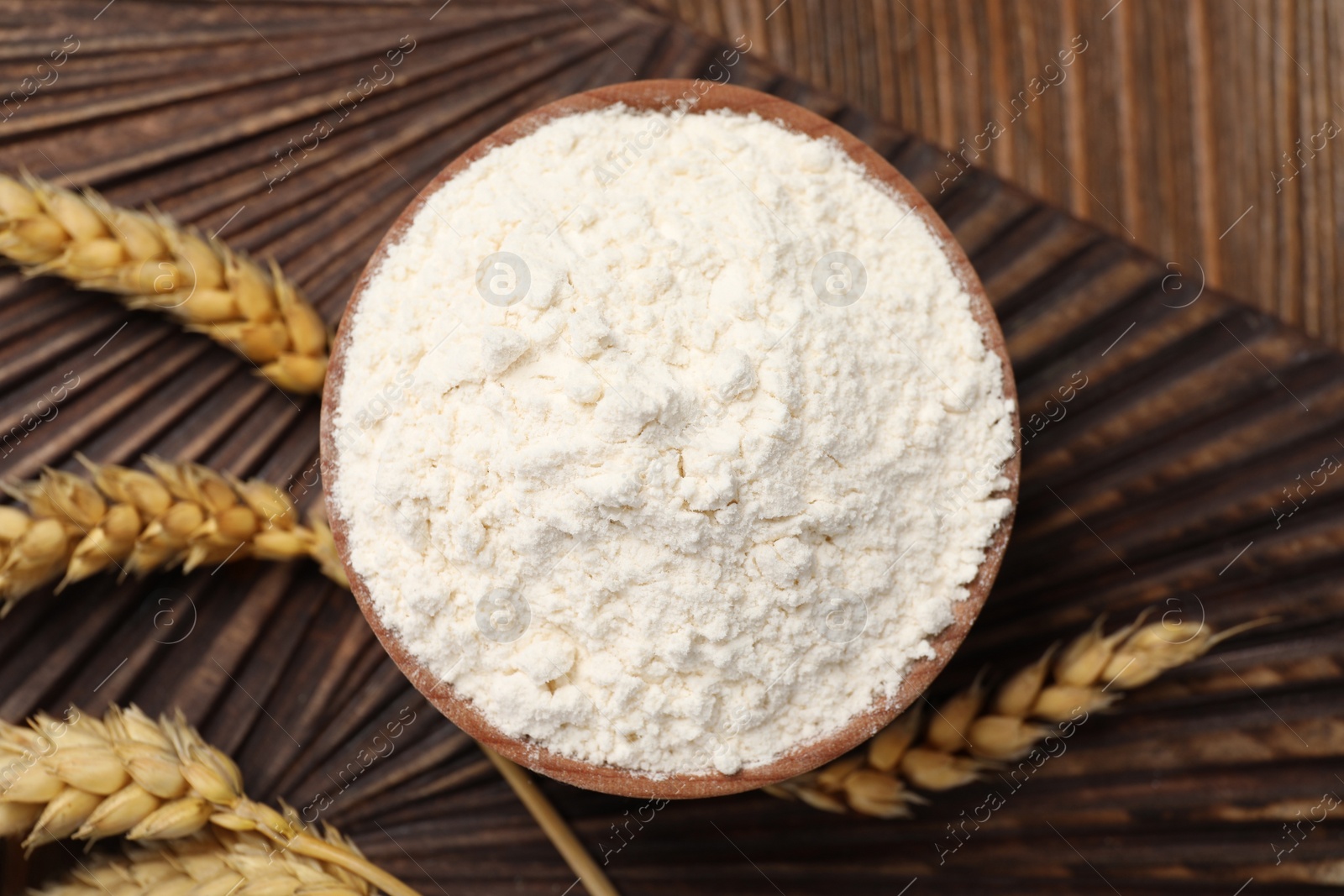 Photo of Bowl of organic wheat flour on wooden table, flat lay