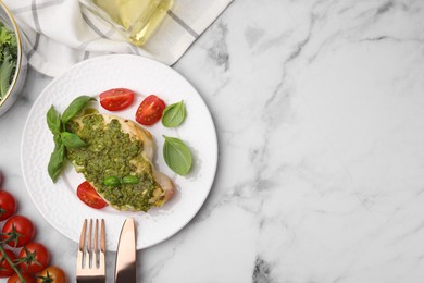 Delicious chicken breast with pesto sauce, tomatoes and cutlery served on white marble table, flat lay. Space for text