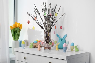 Photo of Beautiful pussy willow branches with paper eggs in vase and Easter decor on white chest of drawers at home