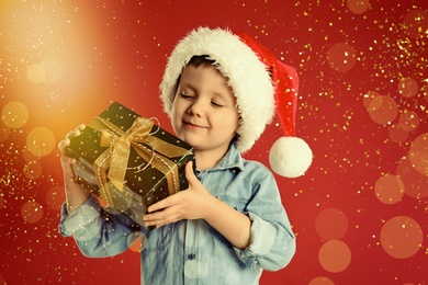 Image of Cute child in Santa hat with Christmas gift on red background