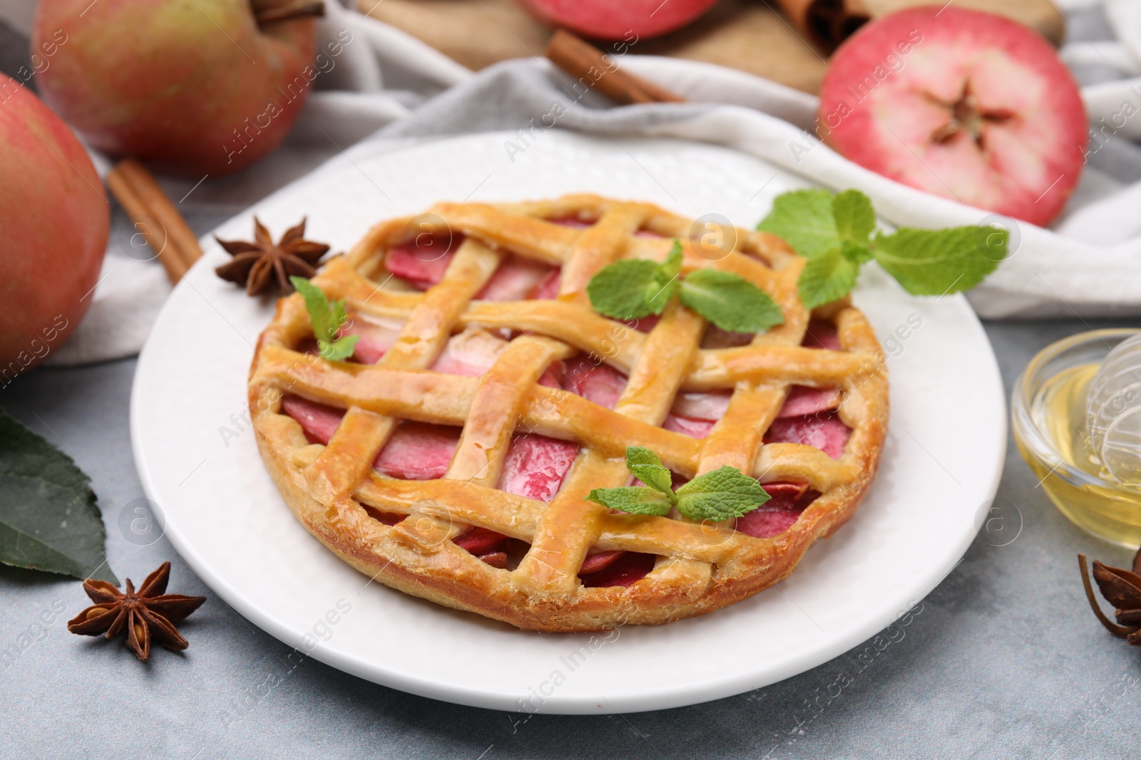 Photo of Delicious apple pie with mint and ingredients on grey table, closeup