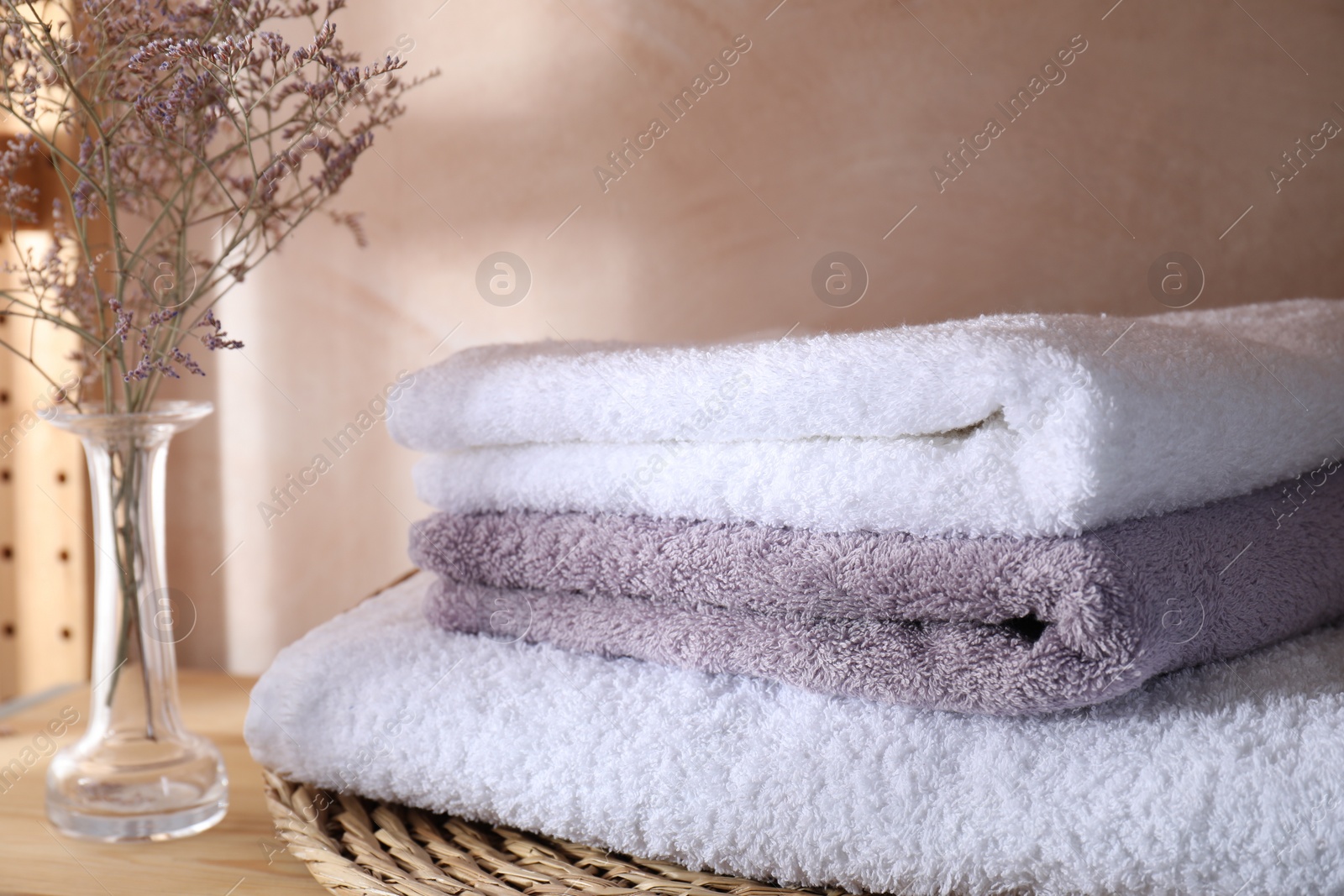 Photo of Stacked soft towels and flowers on shelf indoors, closeup