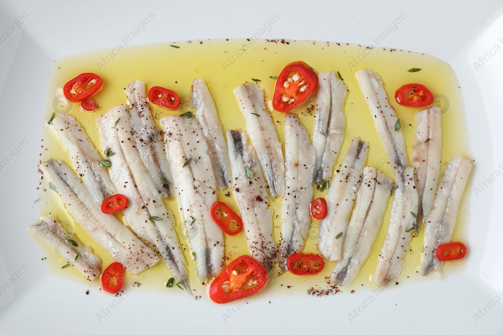 Photo of Tasty pickled anchovies with spices on plate, top view