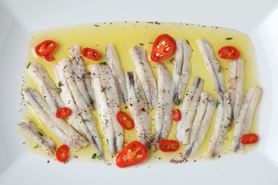 Tasty pickled anchovies with spices on plate, top view