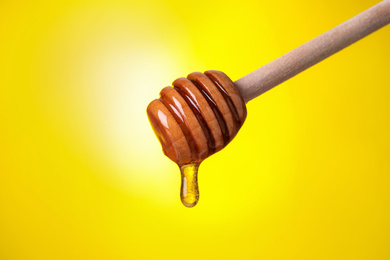 Photo of Dripping honey from dipper on yellow background, closeup