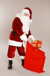 Photo of Authentic Santa Claus with sack and gift on grey background