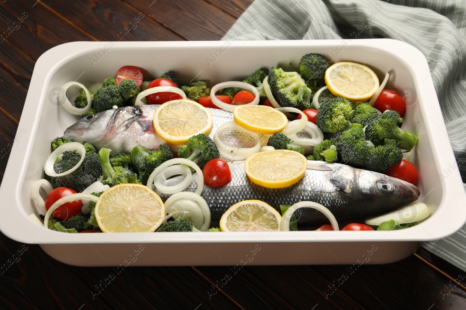 Photo of Raw fish with vegetables and lemon in baking dish on wooden table