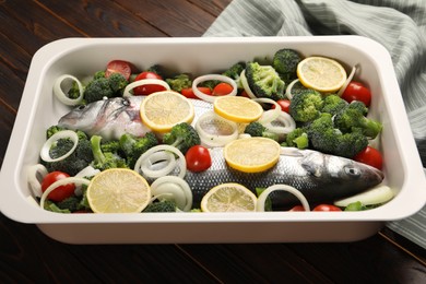 Photo of Raw fish with vegetables and lemon in baking dish on wooden table