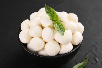 Tasty mozzarella balls and basil leaves in bowl on black table, closeup