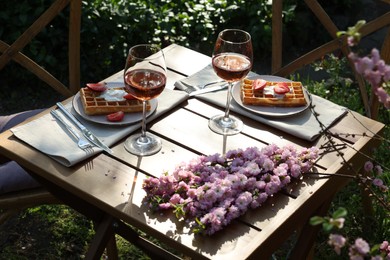 Photo of Delicious Belgian waffles with fresh strawberries and wine served on table in spring garden