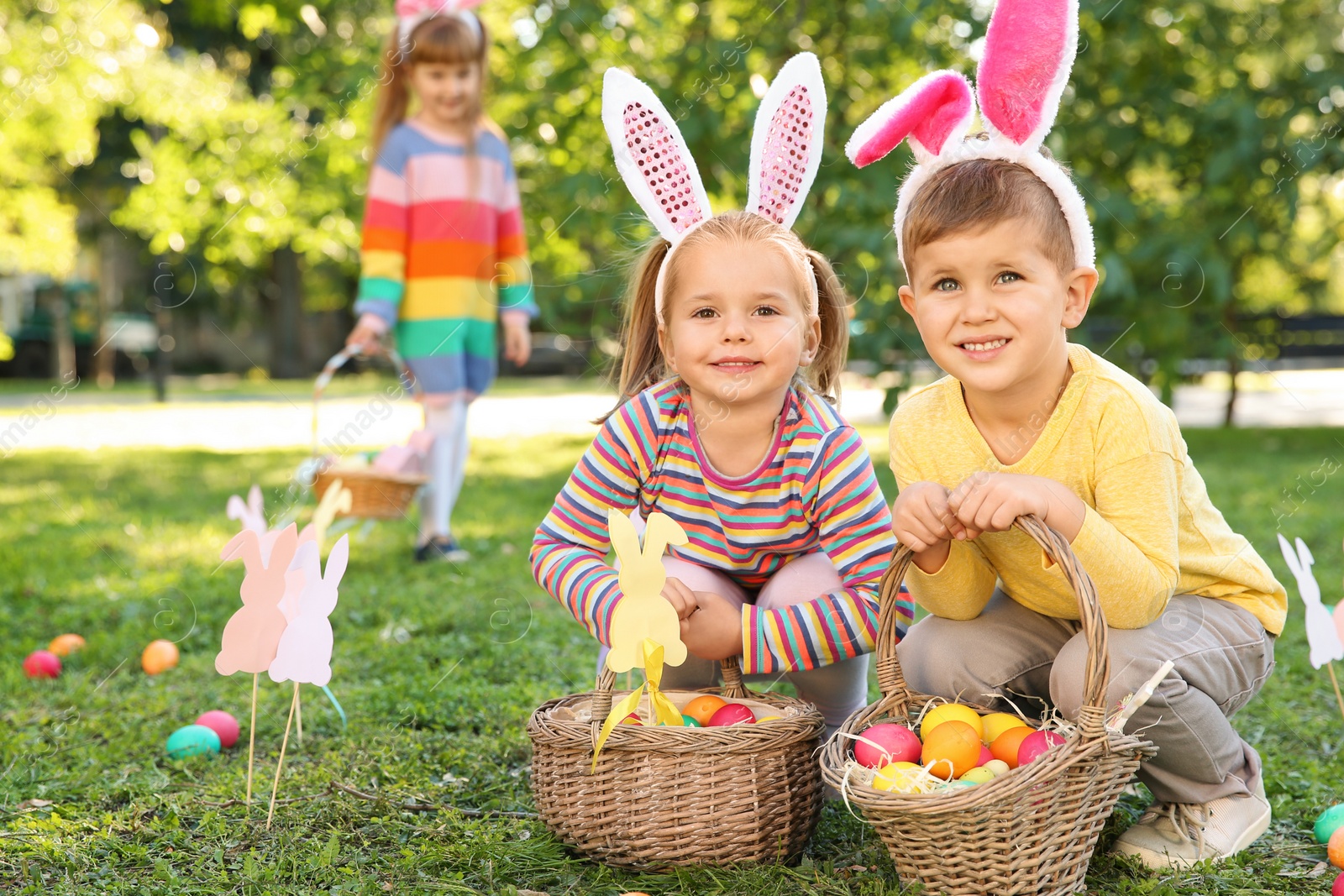 Photo of Cute little children hunting eggs in park. Easter tradition